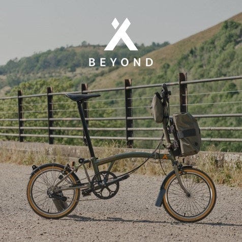 Brompton Beyond Folding Bike with Front and Handlebar Bags on Dirt Road in Front of Fence